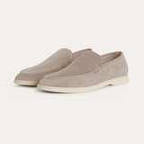 Ein Paar beigefarbene Wildleder-Loafer für Herren mit einer weißen Kontrastsohle, schräg von der Seite fotografiert auf einem weißen Hintergrund.

