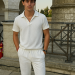 Junger Mann trägt weißes Baumwoll-Sommer-Set mit Polo-Shirt und gerader Hose, inspiriert vom Old-Money-Stil, vor historischer Kulisse