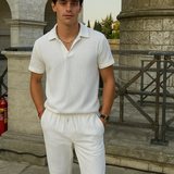 Junger Mann trägt weißes Baumwoll-Sommer-Set mit Polo-Shirt und gerader Hose, inspiriert vom Old-Money-Stil, vor historischer Kulisse