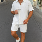 Ein Mann in einem weißen Sommer-Set mit einer 3D-Waffelstruktur, bestehend aus einem Kurzarmhemd und passenden Shorts, geht eine Straße entlang.


